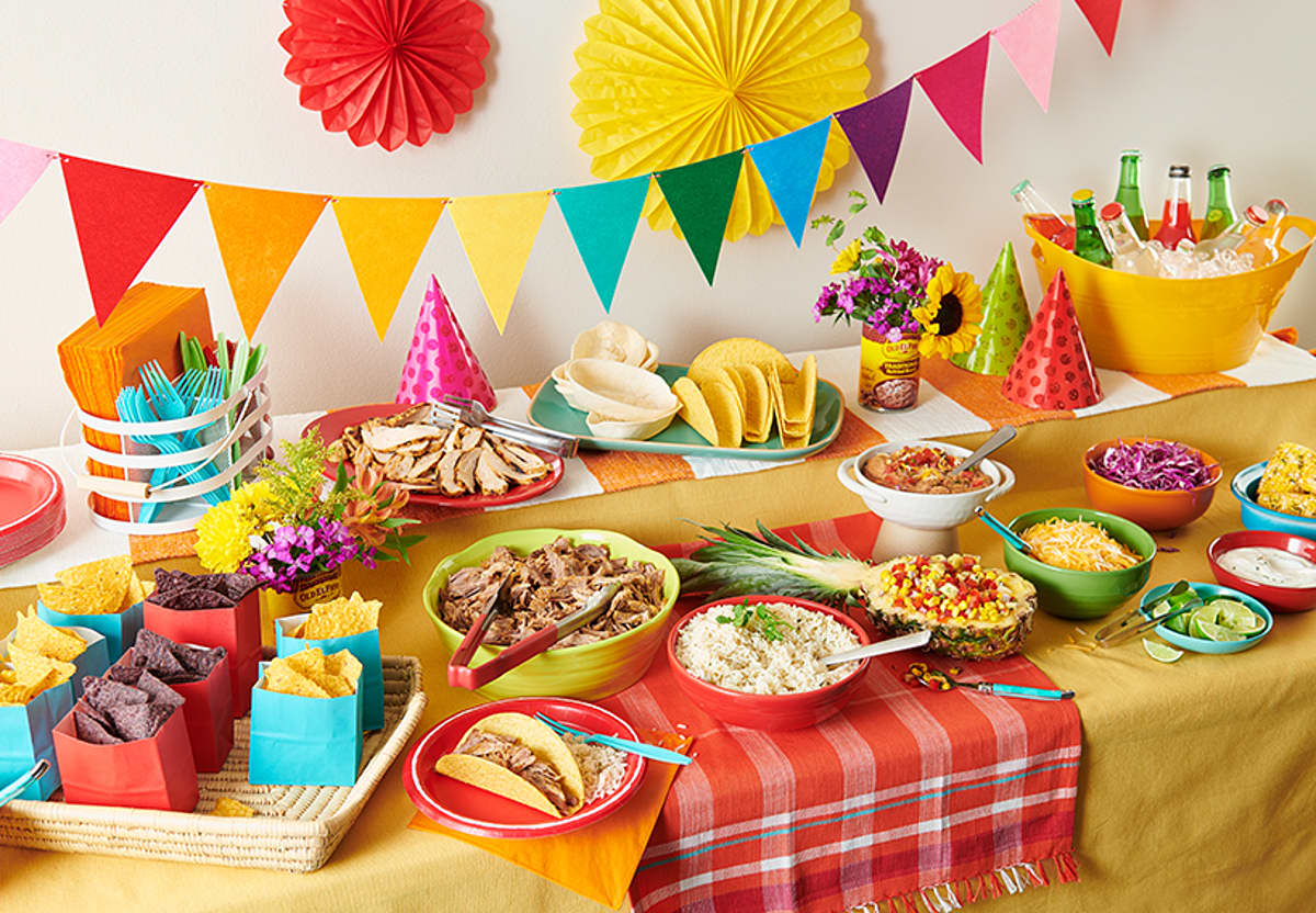 Table with colorful decorations,  party hats, taco shells, chips, drinks, corn, rice, 