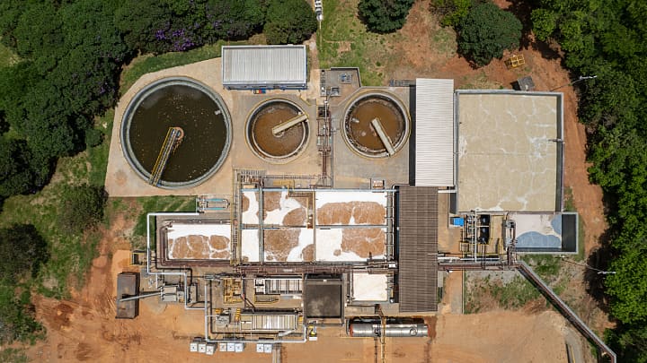 An aerial view of a large water treatment plant featuring multiple tanks and filtration systems, set against a natural landscape with abundant greenery.