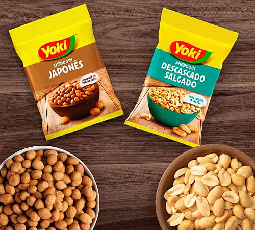 Two packs of Yoki peanuts on a wooden table, with bowls of Japanese peanuts and peeled salted peanuts beside them.