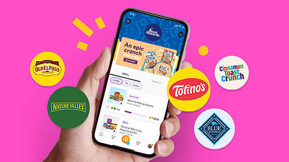 Person holding a phone with several General Mills brand logos displayed on a pink background.