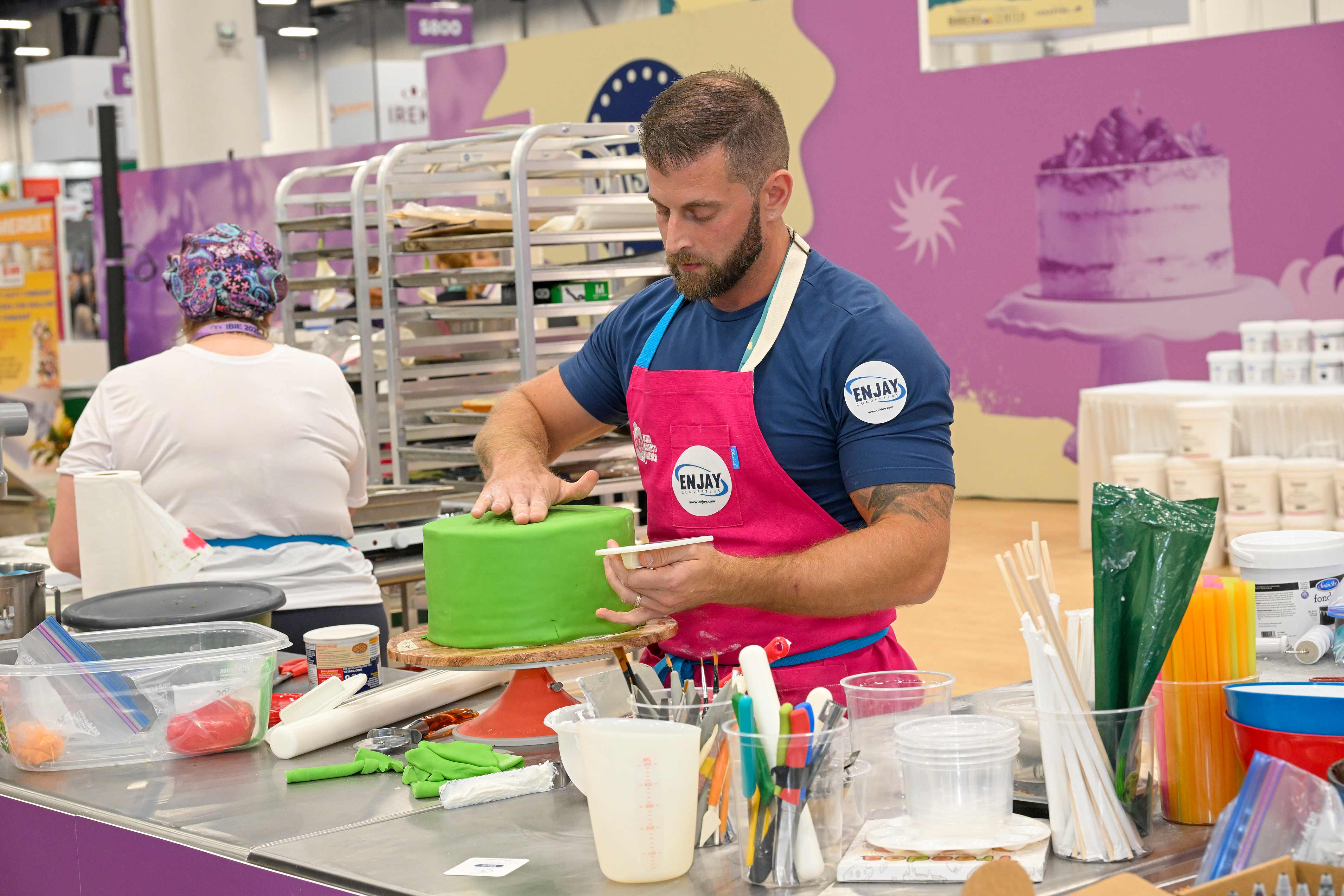 Man in apron decorating a cake with green frosting