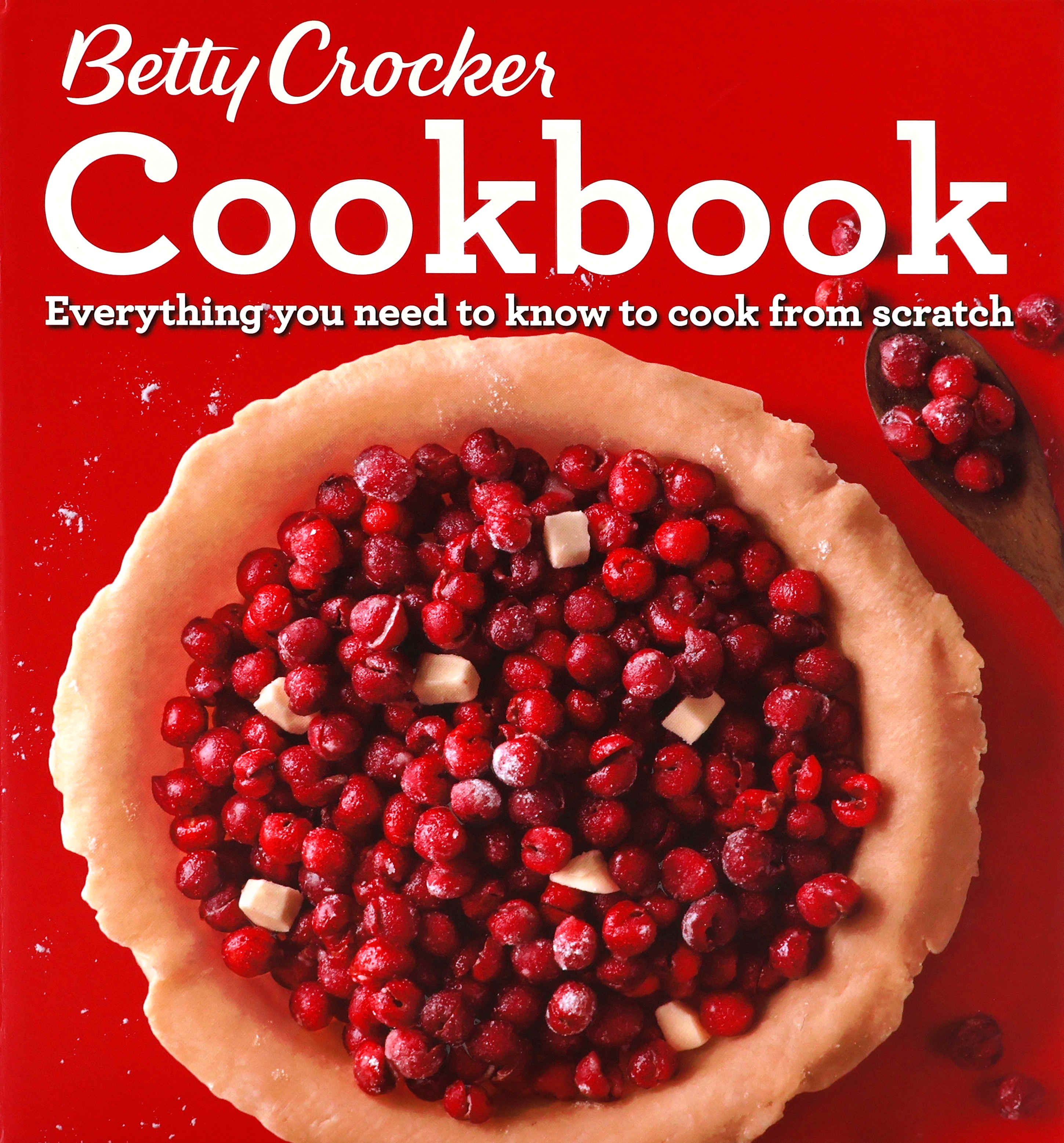 Cover of the 2016 Betty Crocker Cookbook with a red cover that has a photo of an unbaked open-face one-crust cherry pie.  The cherries on the pie are raised/embossed. There is a wooden spoon with cherries lying next to the pie.  “Everything you need to know to cook from scratch” is written in white under the large “Cookbook” word this is also white.