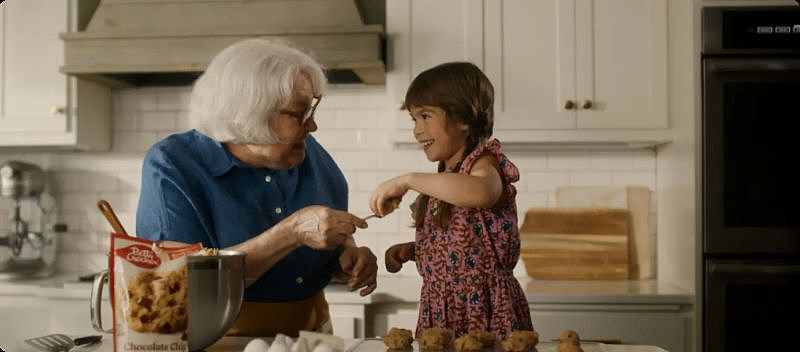 An older adult and a child baking cookies together in a bright kitchen.