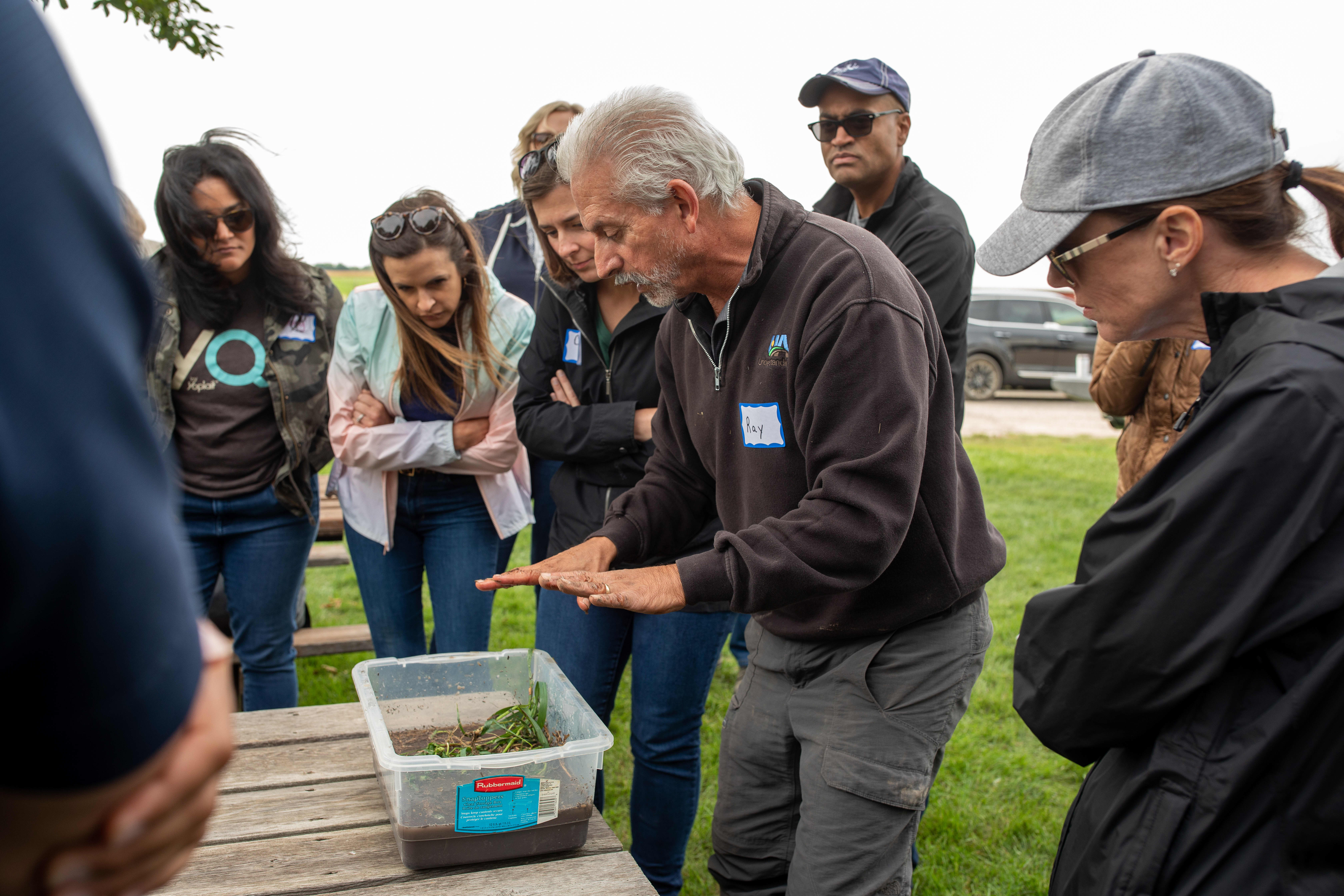 People standing around a box of soil, listening to presenter