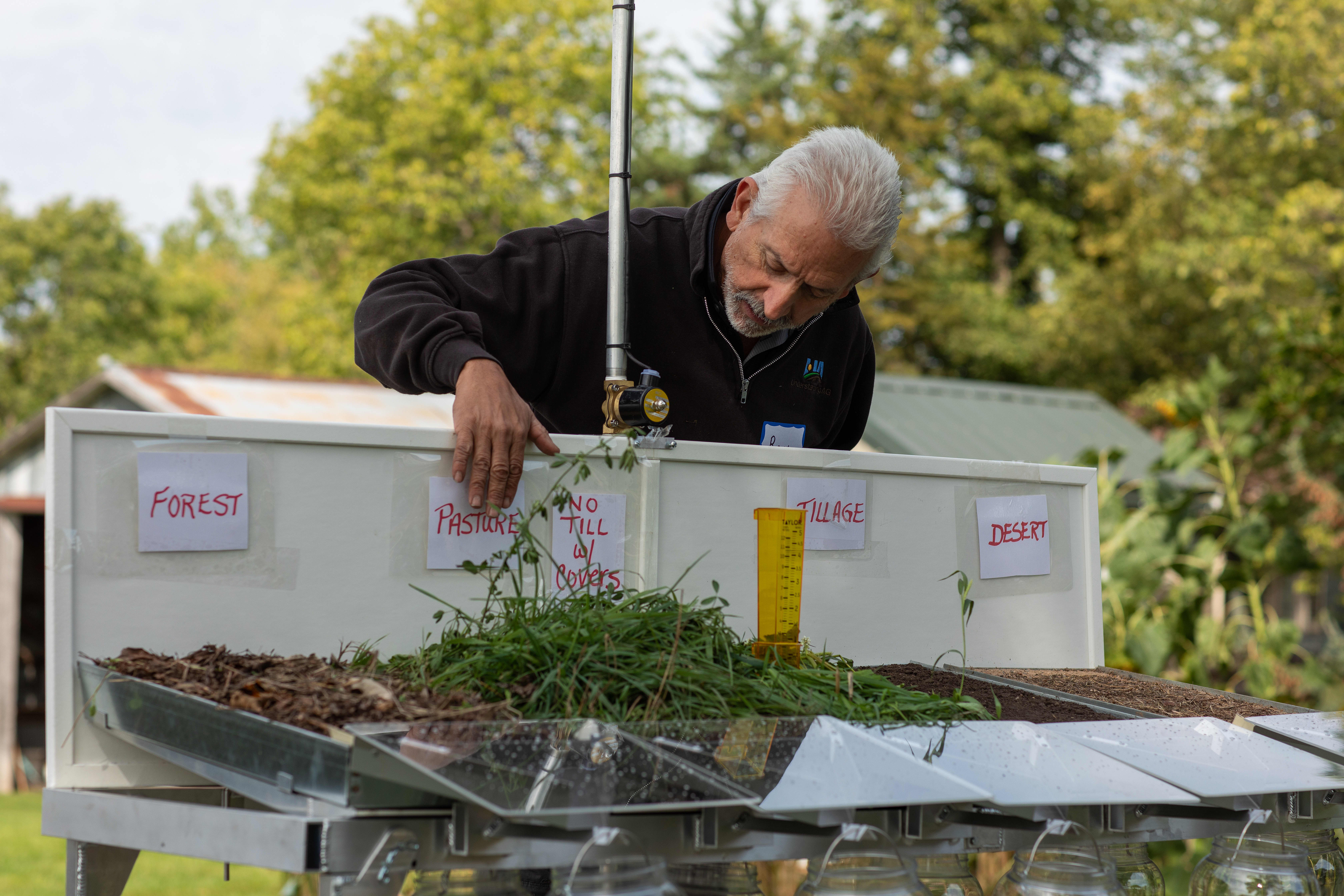 Man with grey hair leaning over a presentation board holding soil samples