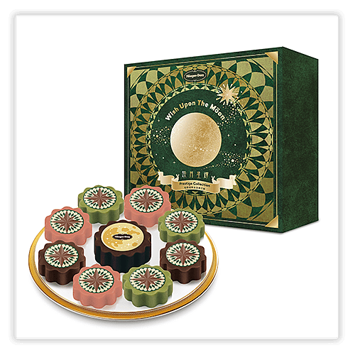 A decorative green and gold box labeled "Wish Upon The Moon" with a circular pattern and a full moon illustration, placed behind a plate of nine mooncakes in pink, green, and brown colors, each featuring intricate designs on top.