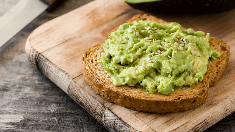avocado toast made with whole grain bread & mashed avocado placed on a wooden board