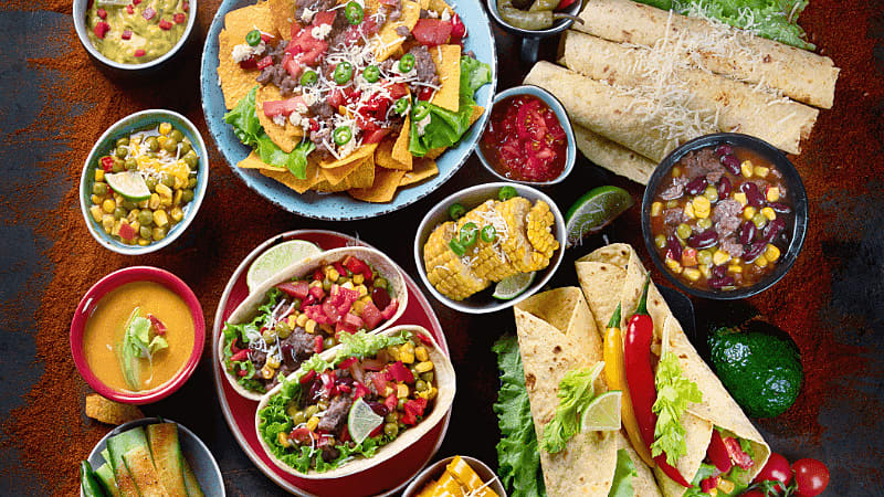 a colourful spread of Mexican food, including tacos, nachos, burritos, corn, guacamole, salsa & cheese dip