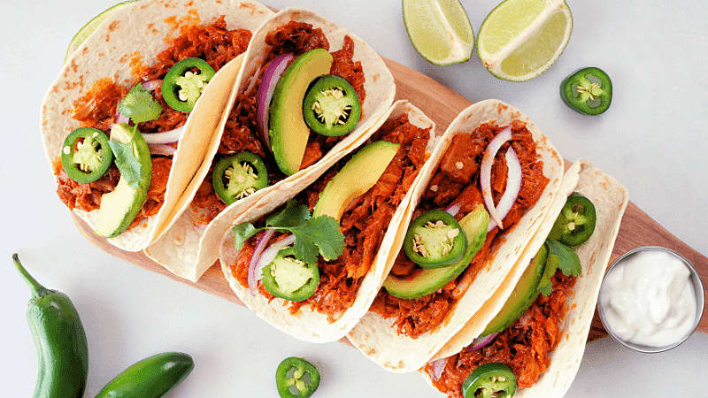 steak fajitas topped with sliced jalapenos served on a plate surrounded by lime wedges & sour cream