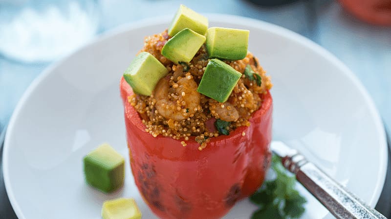 stuffed red bell pepper topped with diced avocados served on a white plate