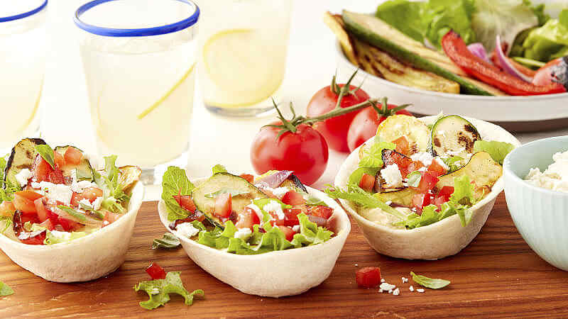 Les bols souples Old El Paso remplis d'une variété de légumes grillés sur une planche de service en bois