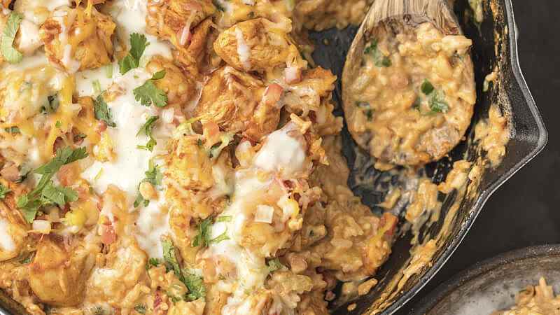 A skillet of chicken con queso with a wooden spoon