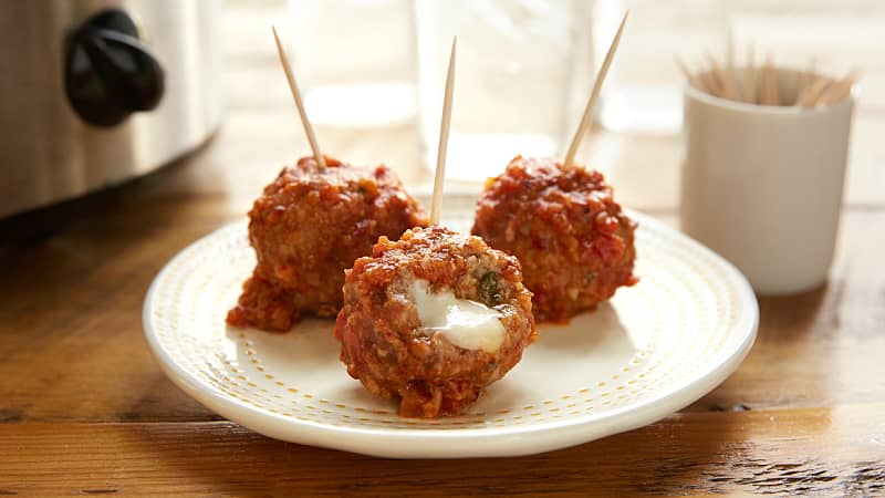 Three beef meatballs stuffed with cheese on a white plate on a wooden table.