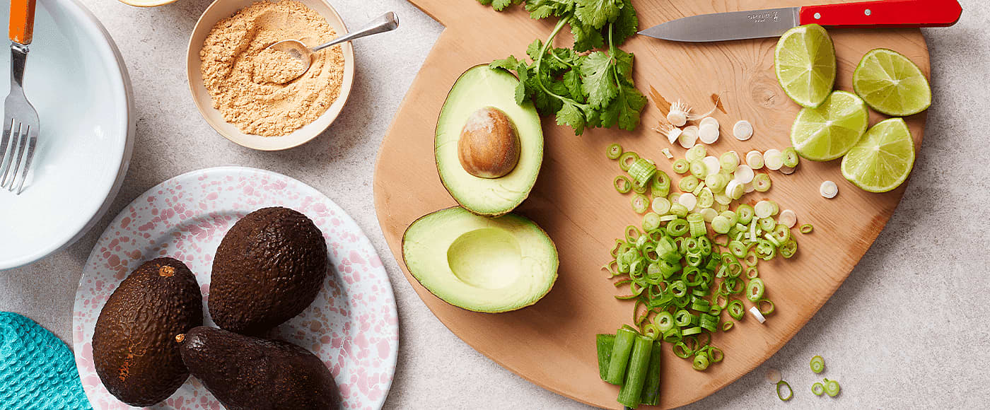 avocados, spring onion, cilantro & lime slice placed on chopping board